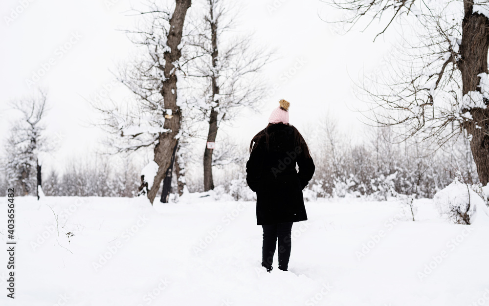 Rear view of brunette woman walking in snowy park in snowfall