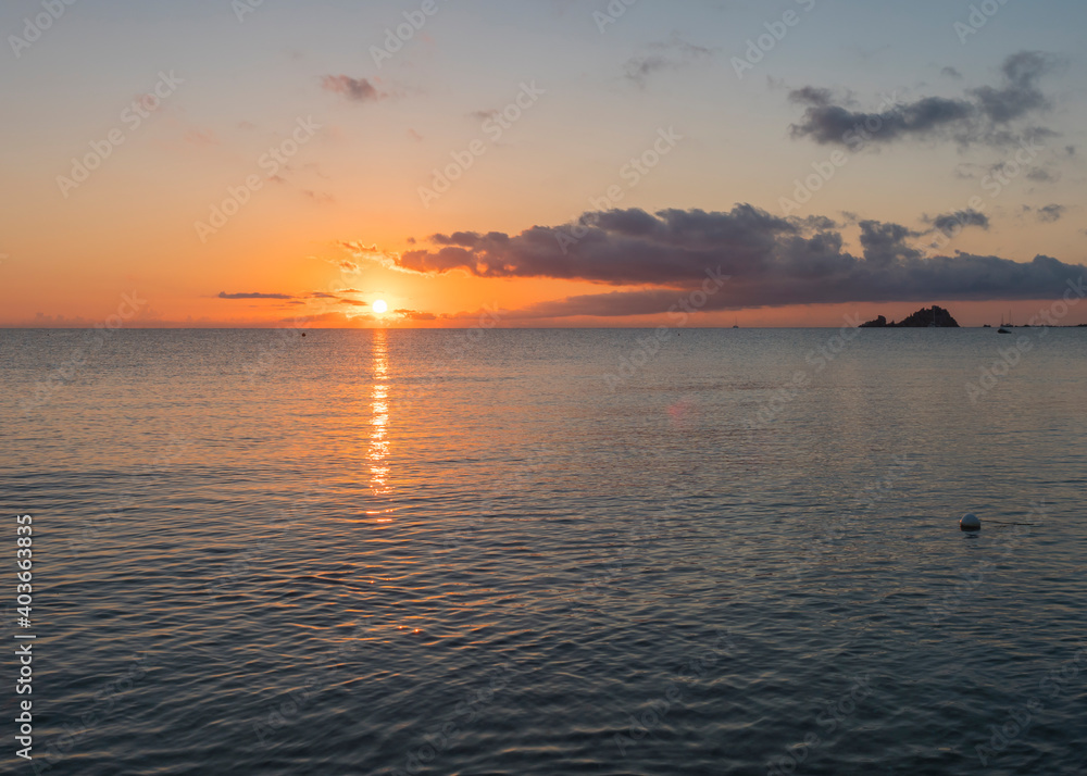 Naklejka premium Sunrise with the red orange sun raising up from the sea with dark clouds at beach Spiaggia di Santa Maria Navarrese, Sardinia, Italy