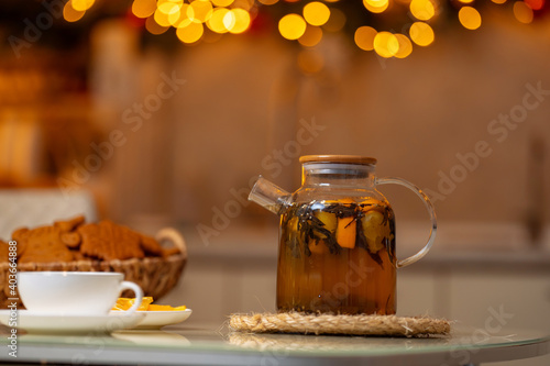 Black tea with orange, ginger and cinnamon in a glass teapot. decorated kitchen.
