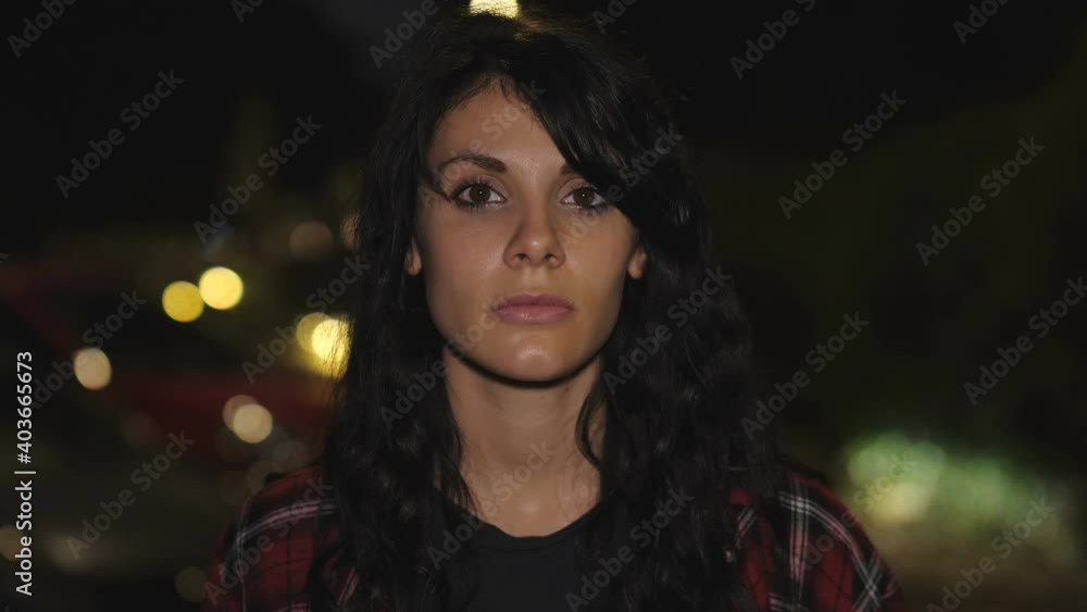 thoughts, concern - young woman in the city at night stares serious at camera thoughts, concern - young woman in the city at night stares serious at camera