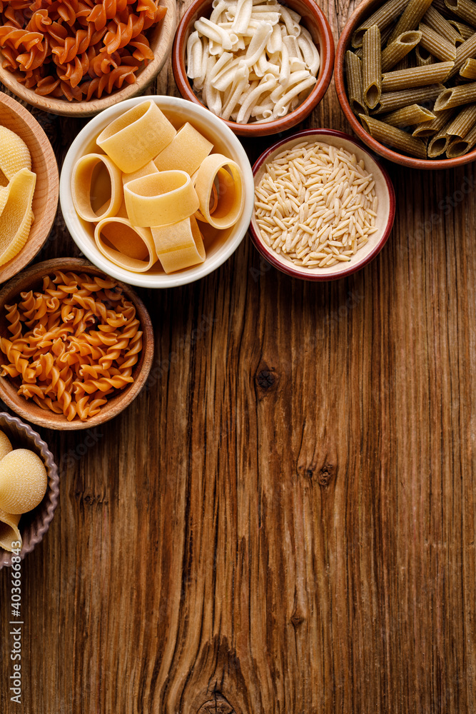 Different types of pasta in a bowls on a wooden background with copy space