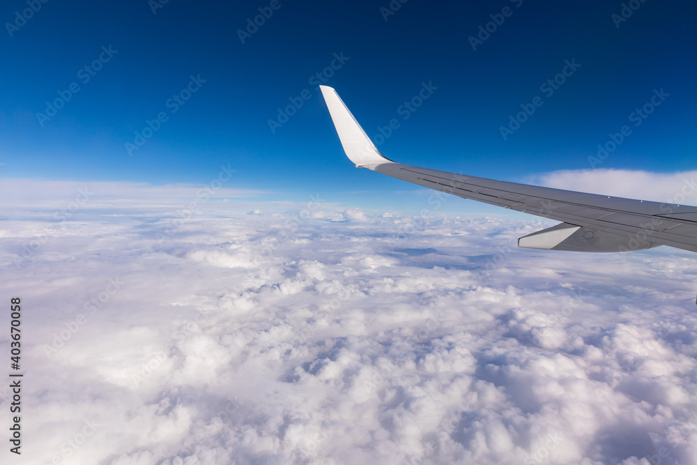 Obraz premium View of the wing of an airplane flying above the clouds at high altitude under a blue sky from the passenger window. In flight over Europe. View of jet airplane wing flying in blue sky over clouds.