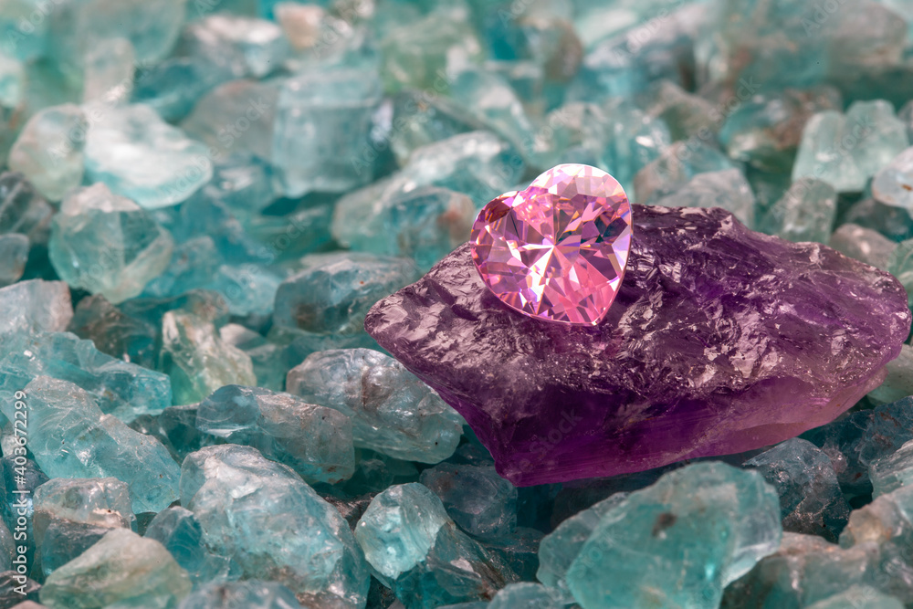 pink garnet heart shaped on raw garnet stones in the midst of raw sky blue gemstones.. pink garnet heart shaped on raw garnet stones in the midst of raw sky blue gemstones..