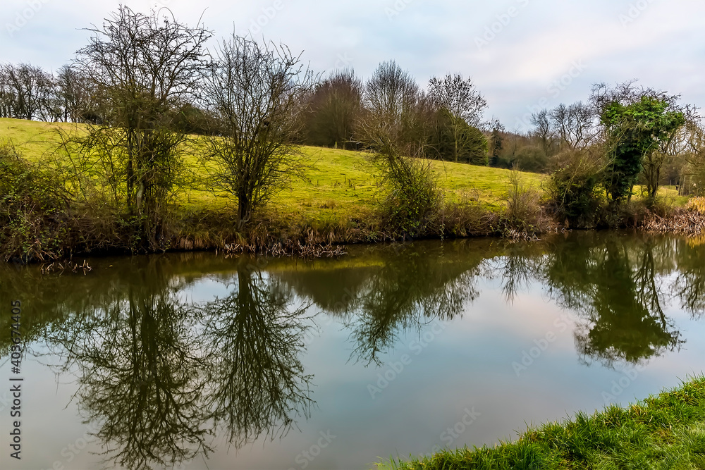 Trees lining the Grand Union Canal near Foxton Locks, UK are reflected in the water on a still winter's afternoon