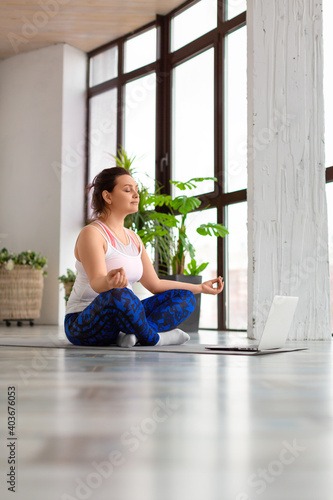 Woman meditate in front of laptop in home interior. Healthy lifestyle concept. Vertical photo.