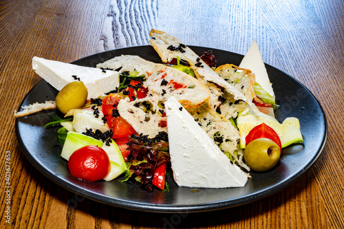 Salad on a plate. Salad with cheese, bread, ofochas and fruits on a black plate.