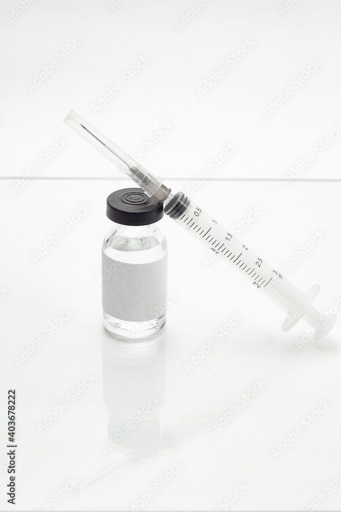Vidro de vacina e seringa sobre a superfície branca de uma mesa.