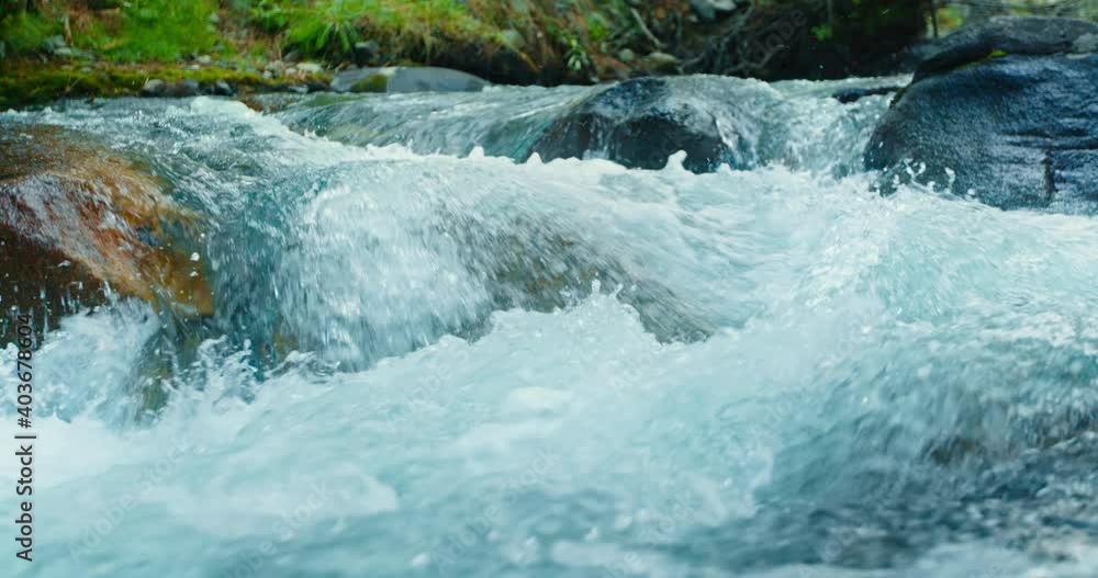 Closeup water flowing through rocks in river. River stream splashing above stones. Small waterfall in spring at daytime Closeup water flowing through rocks in river. River stream splashing above stones. Small waterfall in spring at daytime