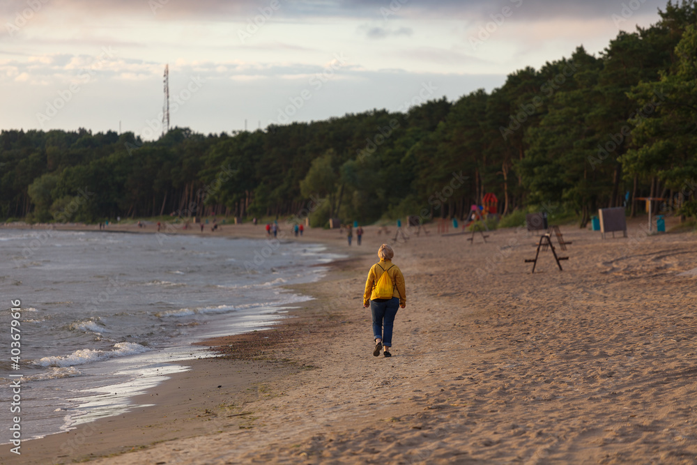 Woman is walking by the shore of Baltic sea. Windy summer day.
