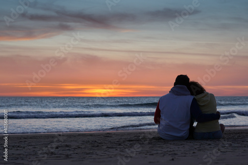 Silhouette of a couple in love sitting together watching the sunset on the beach.