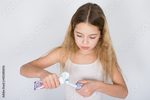 Young girl put toothpaste on rotating-oscillating electric toothbrush isolated on white background. Oral hygiene and white teeth concept.