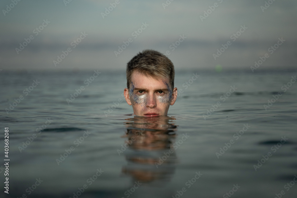 portrait of a man with sequins on his face swimming in the sea