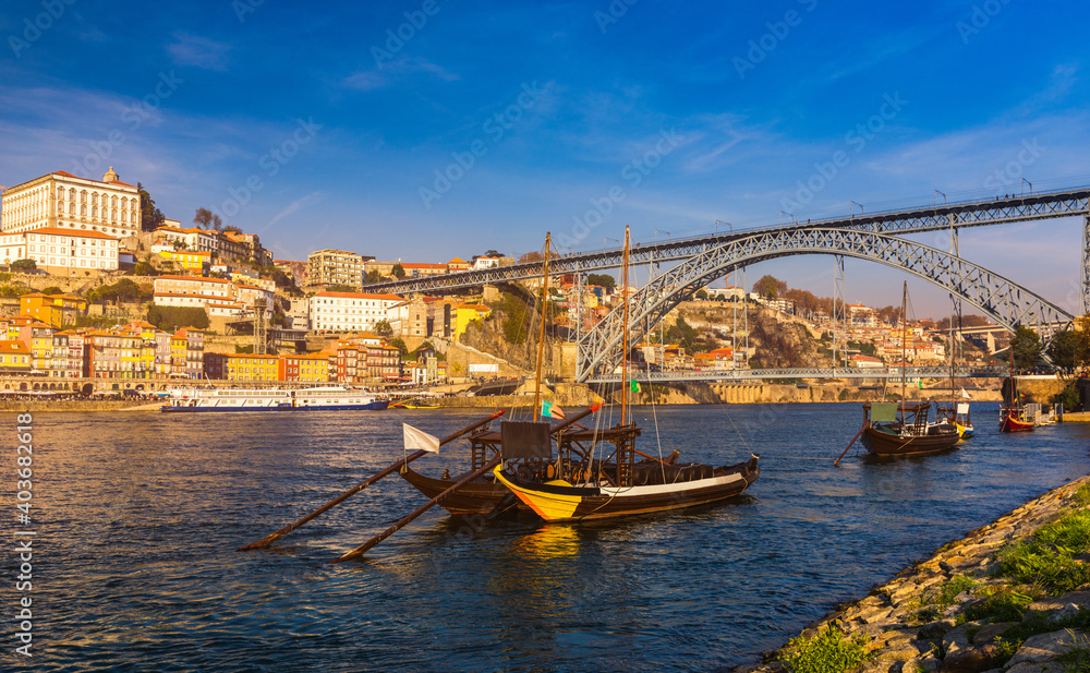 Obraz premium Port wine boats at the waterfront with Dom Luis bridge and the old town on the Douro River in Ribeira in the city centre of Porto in Porugal in Europe. Portugal, Porto