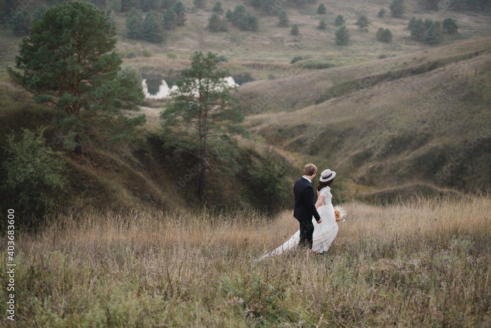 Obraz premium Romantic, young and happy caucasian couple in wedding clothes on the background of beautiful nature. Love, relationships, romance, happiness concept. Bride and groom traveling together.