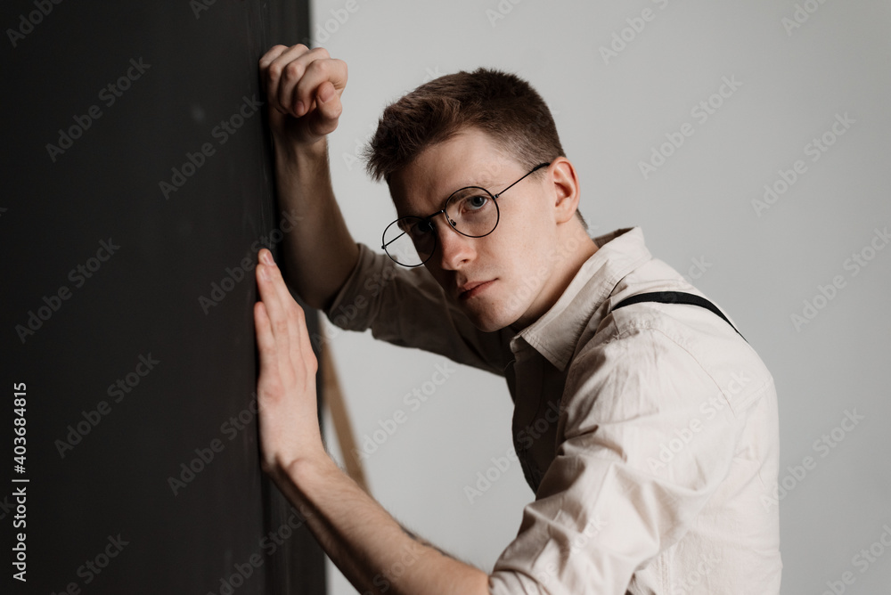 portrait of a young guy in round glasses standing against a black wall