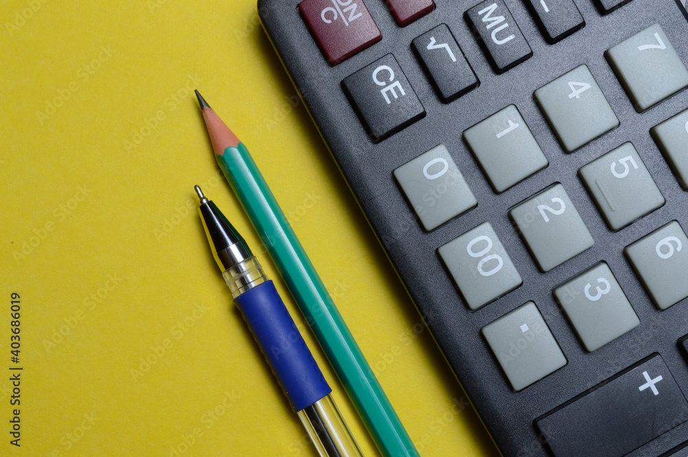 calculator pencil and pen on a yellow background. close-up. calculator pencil and pen on a yellow background. close-up.