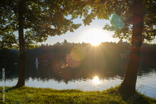 Słońce zachodzi z flarą i promieniami między drzewami nad jeziorem latem w ciepły wakacyjny dzień z kempingiem w tle