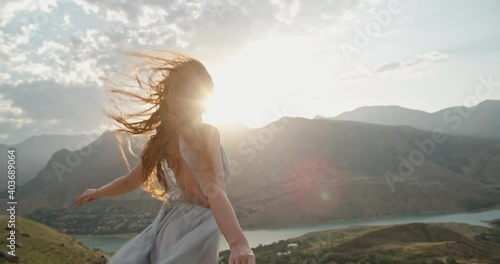 Woman in white dress standing on top of a mountain with raised hands while wind is blowing her dress and red hair - freedom, nature concept 4k footage photo