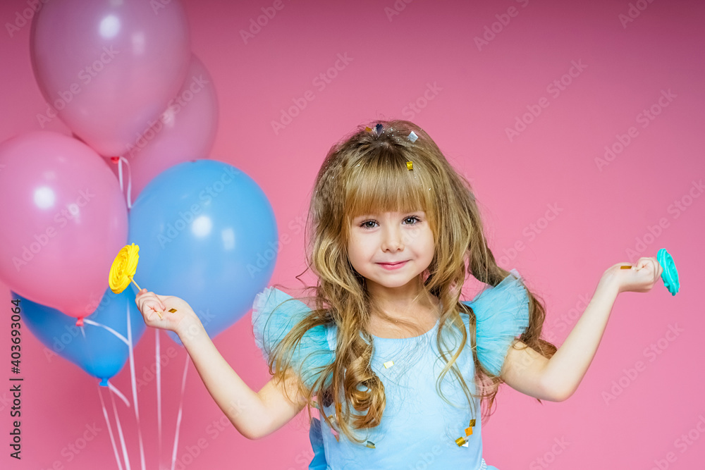 Child's holiday. Girl smiles on a background of pink background and balloons and holds candy
