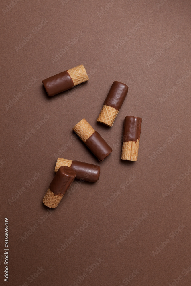 Crispy wafer rolls half-coated in milk chocolate. Top view, brown background, copy space