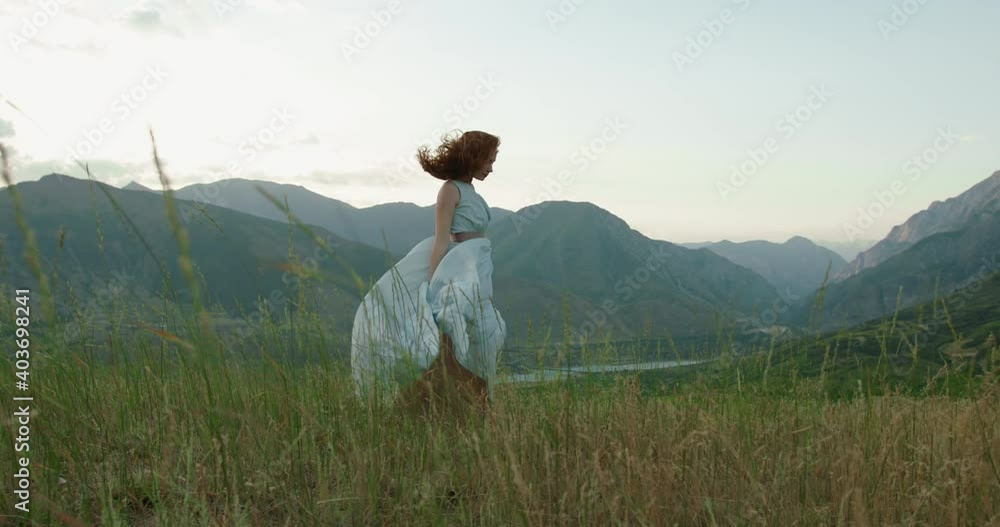 Girl in light dress with red hair is walking on top of a spring mountain with scenic view. Woman in search for inspiration - freedom concept 4k footage Girl in light dress with red hair is walking on top of a spring mountain with scenic view. Woman in search for inspiration - freedom concept 4k footage