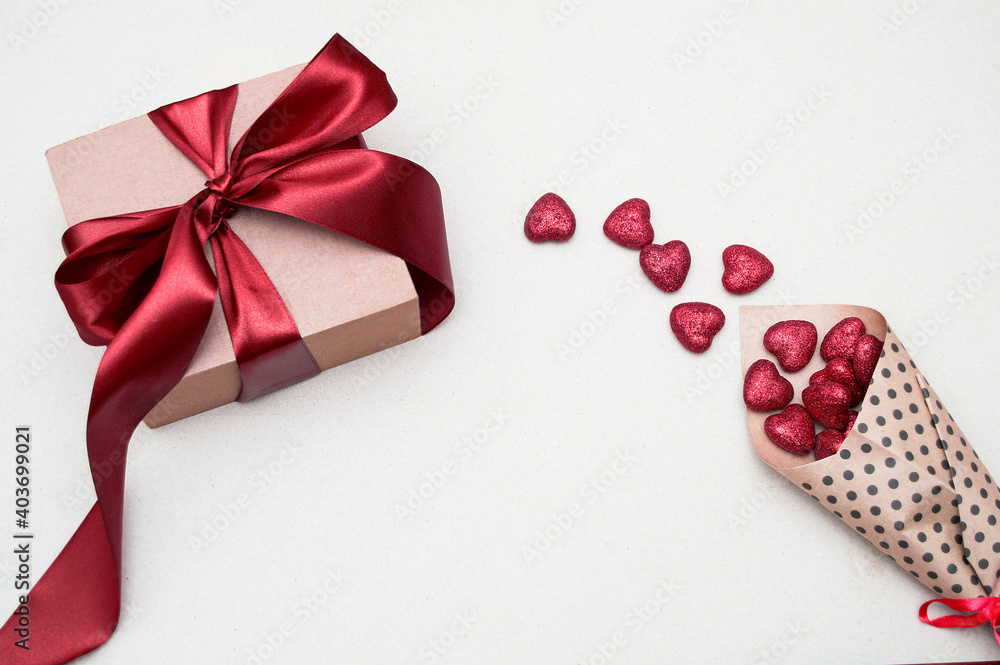 a gift in a craft package with a red bow and red shiny hearts in a paper bag on a light background, vi on top. Valentine's Day card with space for text a gift in a craft package with a red bow and red shiny hearts in a paper bag on a light background, vi on top. Valentine's Day card with space for text