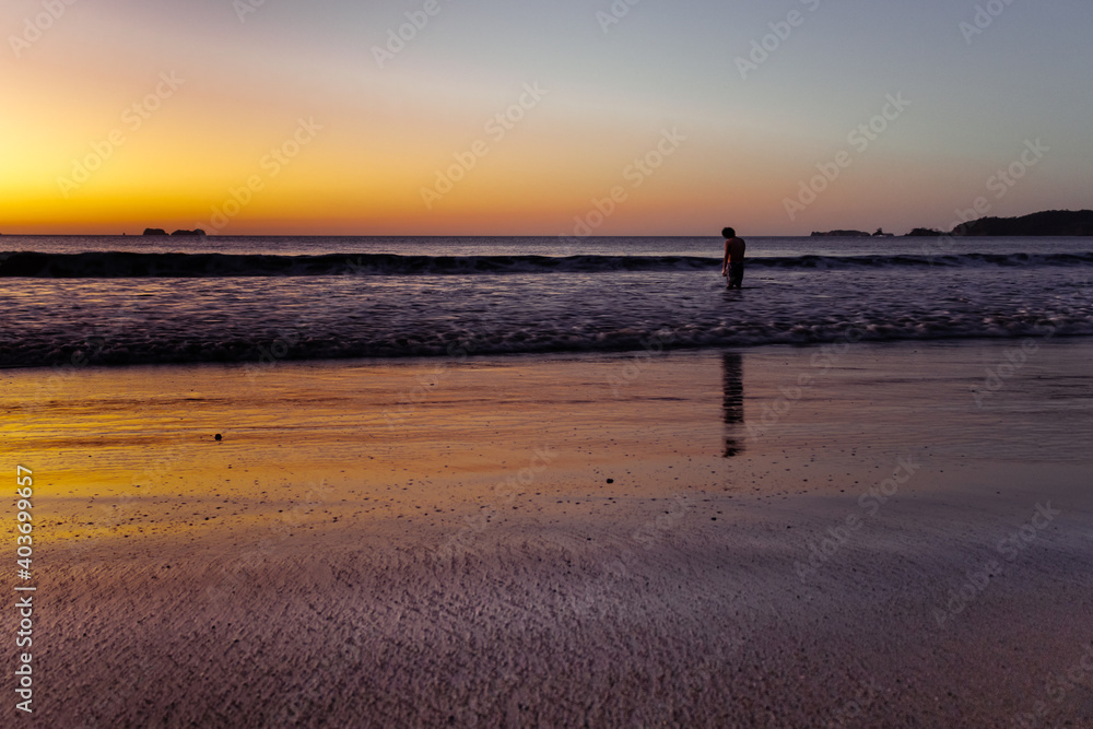 lonely guy walking on the beach at sunset 