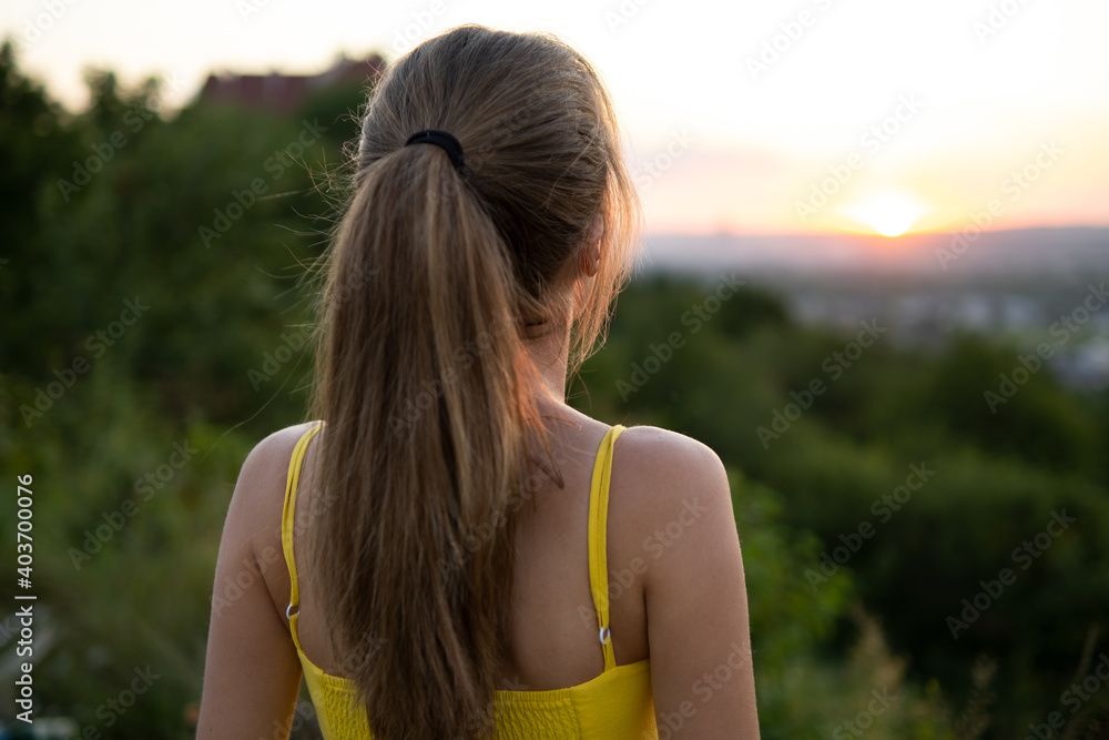 Young woman in yellow summer dress standing in green meadow enjoying sunset view. Young woman in yellow summer dress standing in green meadow enjoying sunset view.