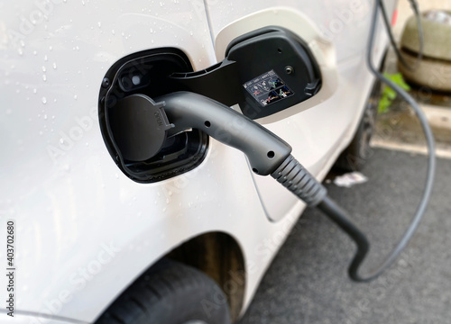 Recharging an electric car with a plug connected to the charging station on a city street. Concept of sustainable and ecological mobility.