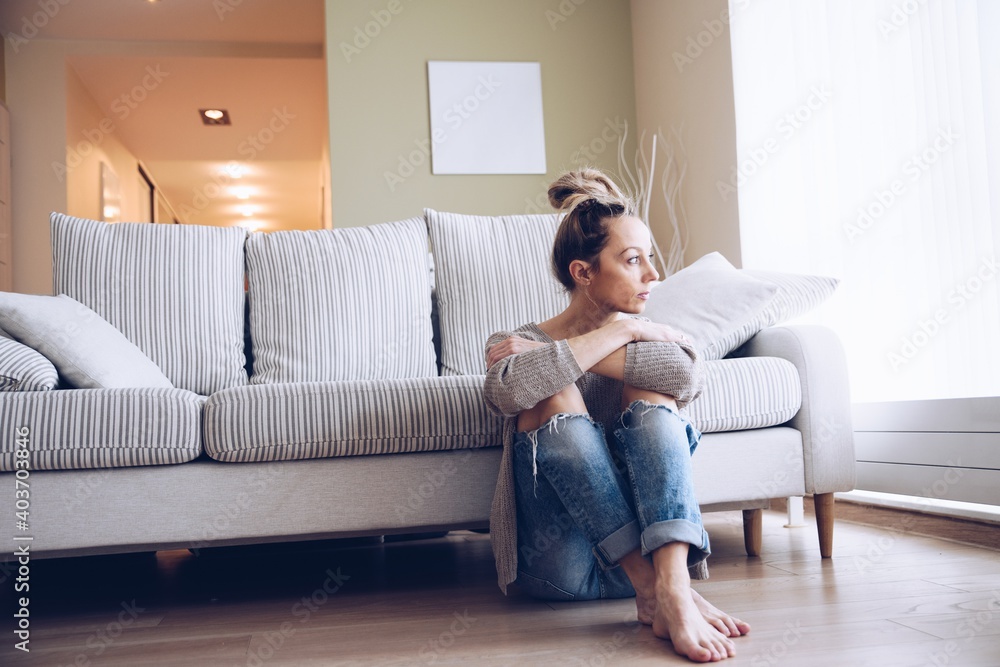 A lonely young woman feels depressed and stressed. She is sitting on the floor. Concept of negative emotions and mental health.