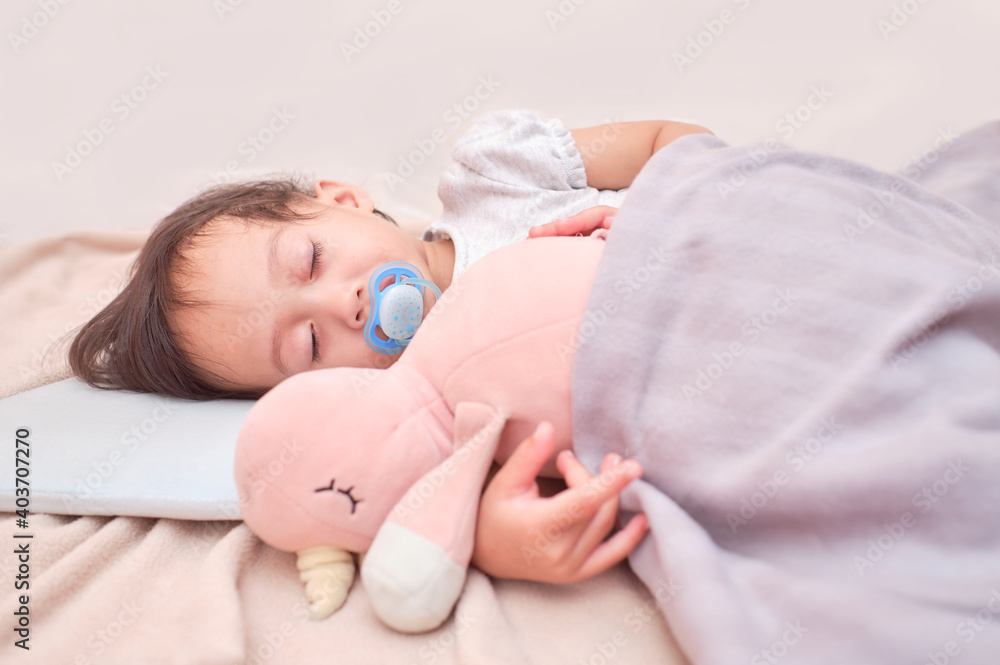 Cute sleepy Asian infant girl sleeping on soft bedding with pacifier, Little kid taking a nap in bed while hugging soft plush fluffy toy wake up with a soother in her mouth Cute sleepy Asian infant girl sleeping on soft bedding with pacifier, Little kid taking a nap in bed while hugging soft plush fluffy toy wake up with a soother in her mouth