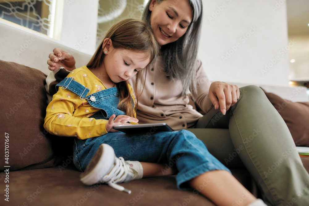 Grandmother sitting next to granddaughter using digital tablet Grandmother sitting next to granddaughter using digital tablet