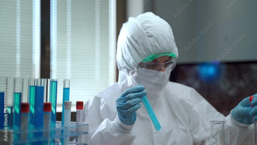 Health care worker in white protective suit working in researching laboratory with hazard solutions and compounds, female chemist using sterile pipette and test tubes, dropping reagent and mixing with Health care worker in white protective suit working in researching laboratory with hazard solutions and compounds, female chemist using sterile pipette and test tubes, dropping reagent and mixing with