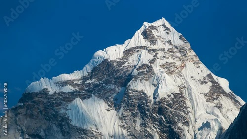 High snowy mountain against the blue sky. Timelapse of the snowcapped peak and light clouds above it. The Himalaya, Nepal photo