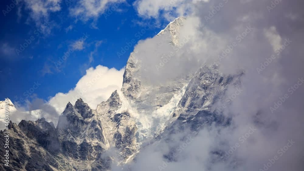 View from below of a high snowy mountain against the blue sky and with clouds on top. View from Phakding, a small village in the Khumbu region of Nepal. Himalaya View from below of a high snowy mountain against the blue sky and with clouds on top. View from Phakding, a small village in the Khumbu region of Nepal. Himalaya