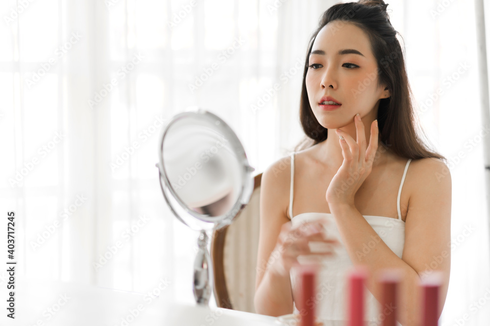 Smiling of young beautiful pretty asian woman clean fresh healthy white skin looking at mirror.girl touching on her face with hand and applying cream at home.spa and beauty concept Smiling of young beautiful pretty asian woman clean fresh healthy white skin looking at mirror.girl touching on her face with hand and applying cream at home.spa and beauty concept