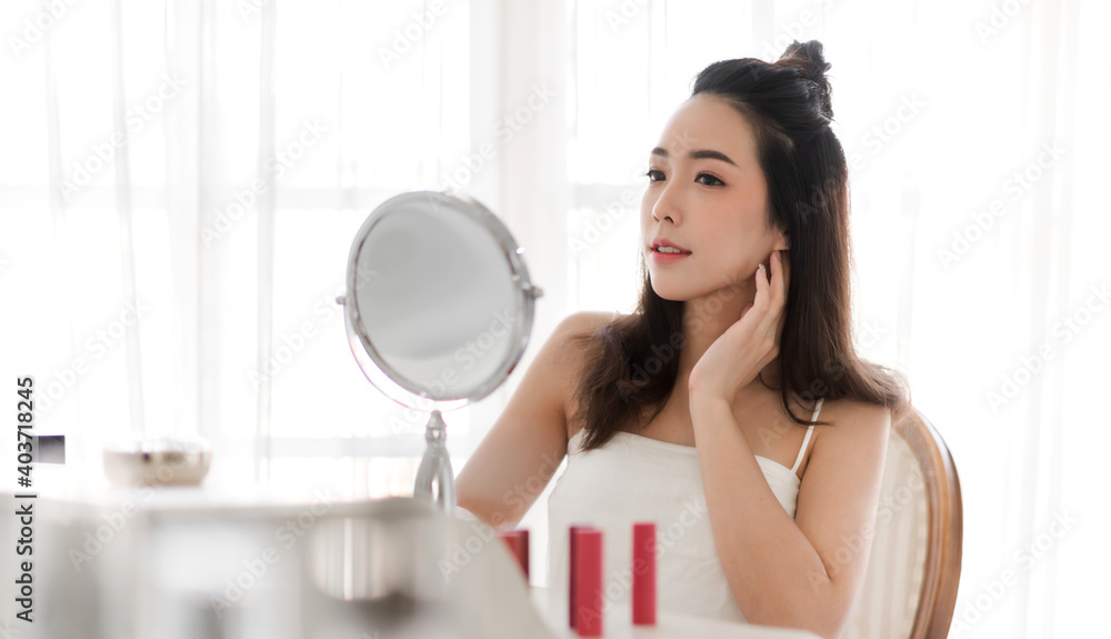 Smiling of young beautiful asian woman clean fresh healthy white skin looking at mirror.girl touching on her face with hand and applying cream at home.spa and beauty concept Smiling of young beautiful asian woman clean fresh healthy white skin looking at mirror.girl touching on her face with hand and applying cream at home.spa and beauty concept