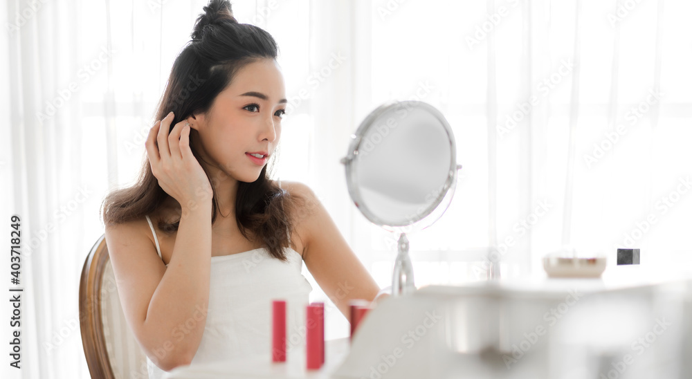 Smiling of young beautiful pretty asian woman clean fresh healthy white skin looking at mirror.girl touching on her face with hand and applying cream at home.spa and beauty concept