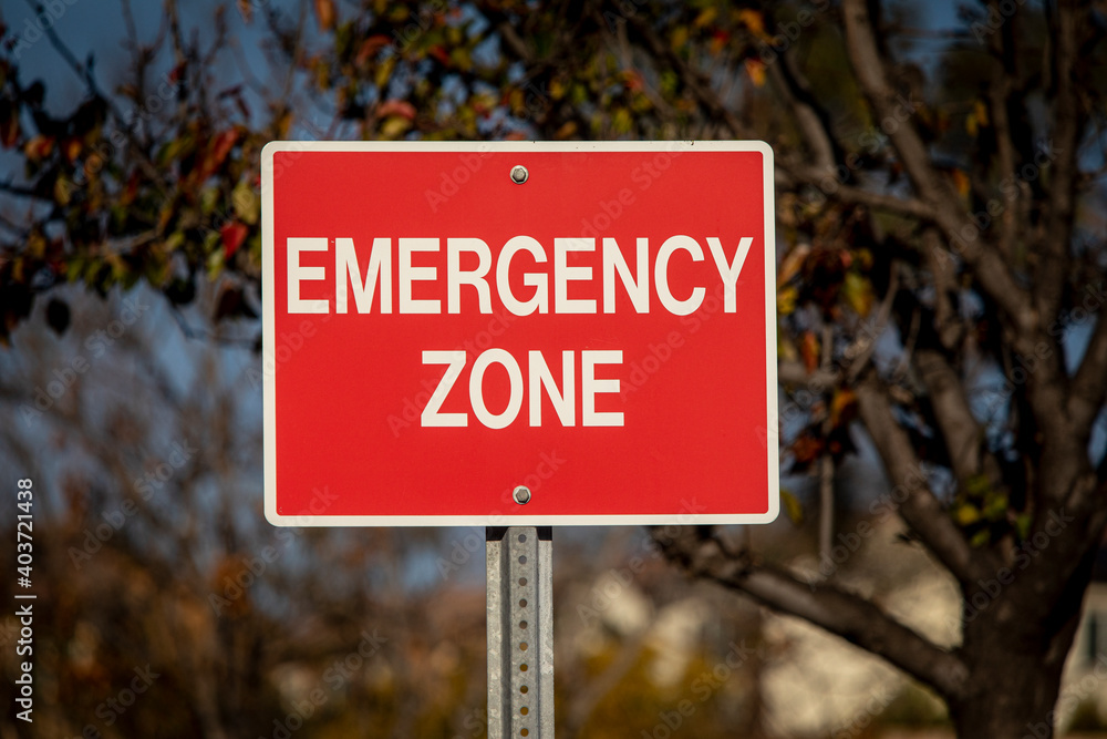 Red sign with white letters stating Emergency Zone against a blue sky Red sign with white letters stating Emergency Zone against a blue sky