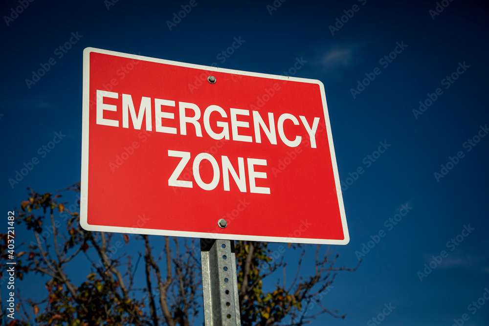 Red sign with white letters stating Emergency Zone against a blue sky Red sign with white letters stating Emergency Zone against a blue sky