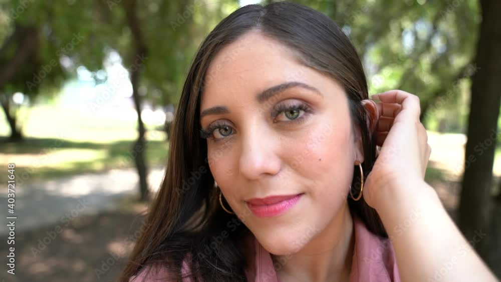 a beautiful latin woman shows her charming smile as her hair rises in the wind in a park near the city a beautiful latin woman shows her charming smile as her hair rises in the wind in a park near the city