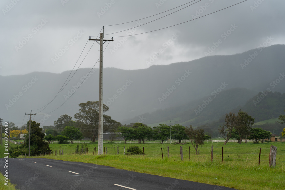 Power line on side of round with clouds coming in over misty foggy green mountains