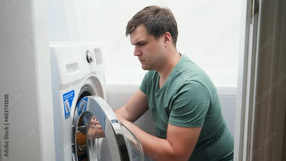 Confused man setting washing laundry machine. Male struggling and frustrating while doing housework and daily routine at home Confused man setting washing laundry machine. Male struggling and frustrating while doing housework and daily routine at home
