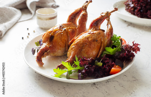 Oven-baked quails with vegetable salad served on white plate close up