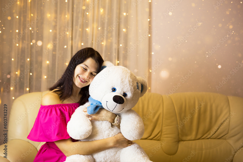 Happy girl in a pink dress hugging a big white soft bear home on the couch. Gift from a loved one, valentine's day, birthday, holiday. Copy space Happy girl in a pink dress hugging a big white soft bear home on the couch. Gift from a loved one, valentine's day, birthday, holiday. Copy space