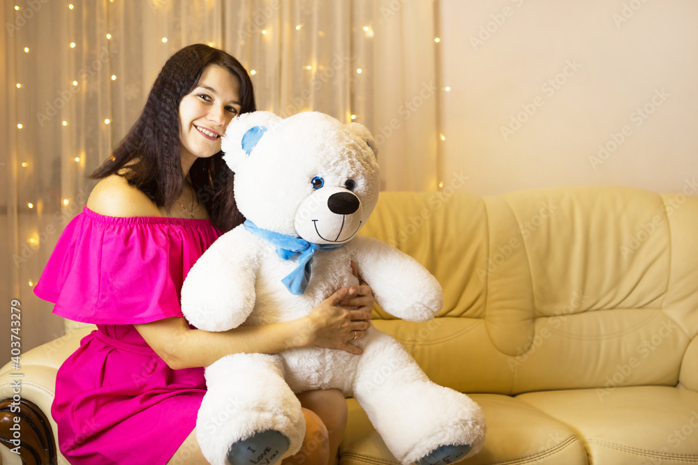 Happy girl in a pink dress hugging a big white soft bear home on the couch. Gift from a loved one, valentine's day, birthday, holiday. Copy space Happy girl in a pink dress hugging a big white soft bear home on the couch. Gift from a loved one, valentine's day, birthday, holiday. Copy space