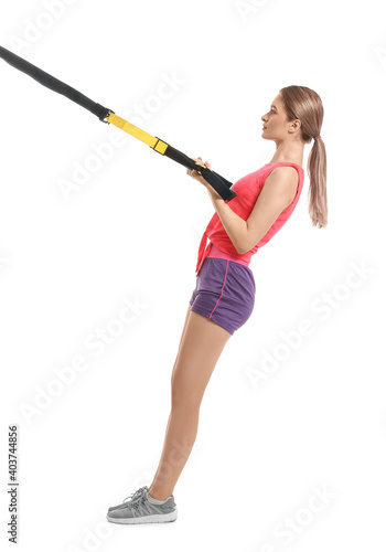 Sporty young woman training with TRX straps on white background