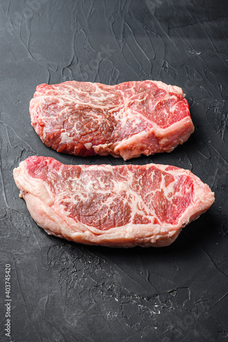 Raw top blade steak cuts, on black textured background side view.