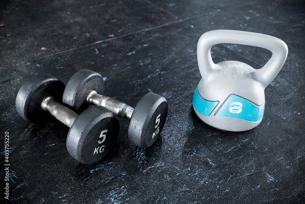 Comparing a pair of dumbbells with a plastic kettlebell. Both lying on the  rubber matting of a gym or fitness center. Stock Photo | Adobe Stock
