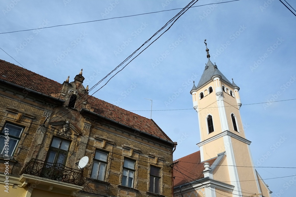 Obraz premium Medieval catholic church near old decorated building on a background of blue sky in Mukachevo, Ukraine. Electricity wires on a foreground.